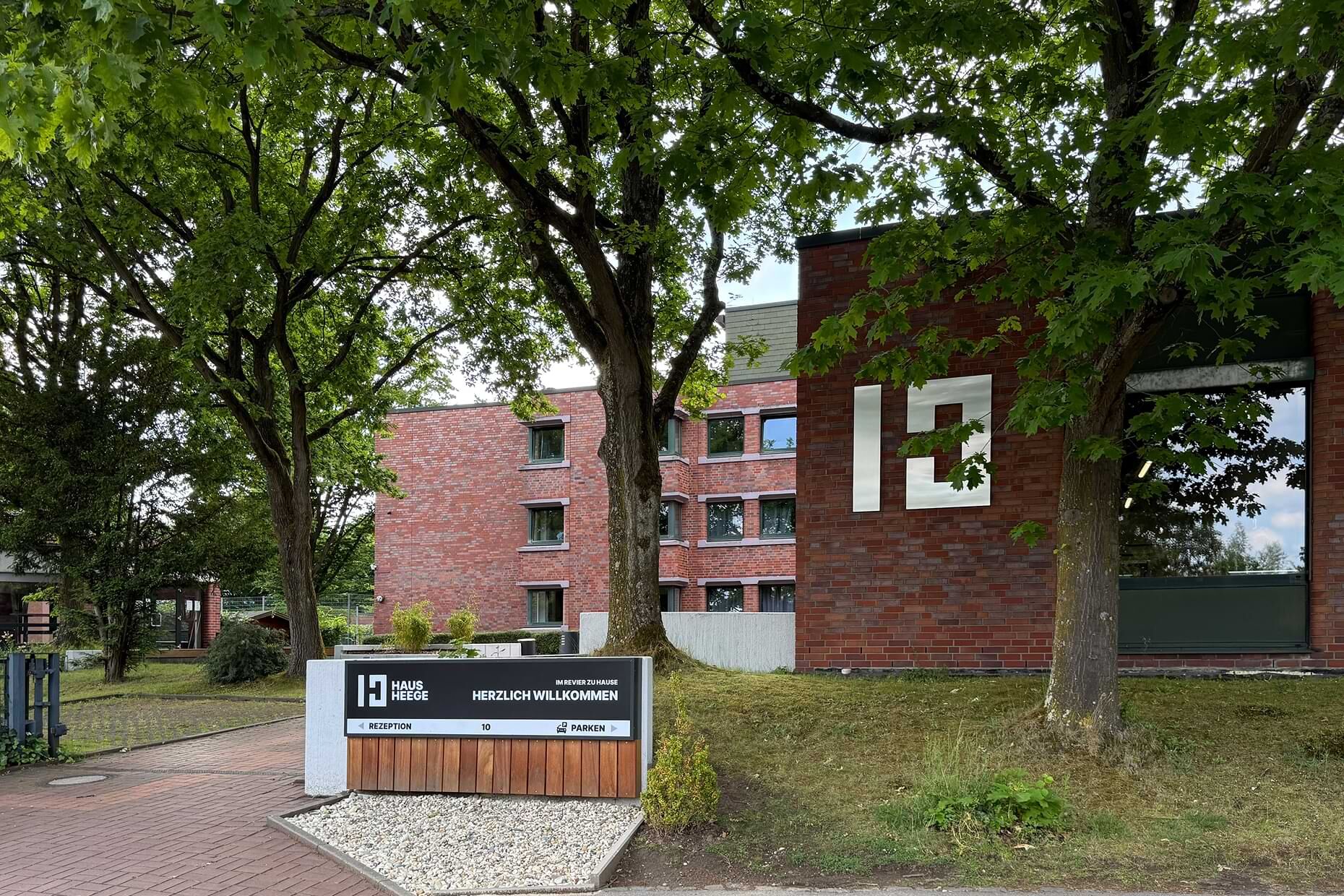 Haus Heege Auffahrt mit Willkommensschild und dem Hauptgebäude des Haus Heege